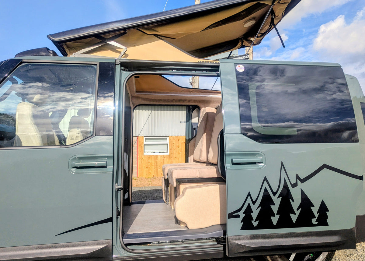 Close-up side view of the Kia PV5 Witley electric campervan with its sliding door open revealing the passenger seating and modular interior layout.