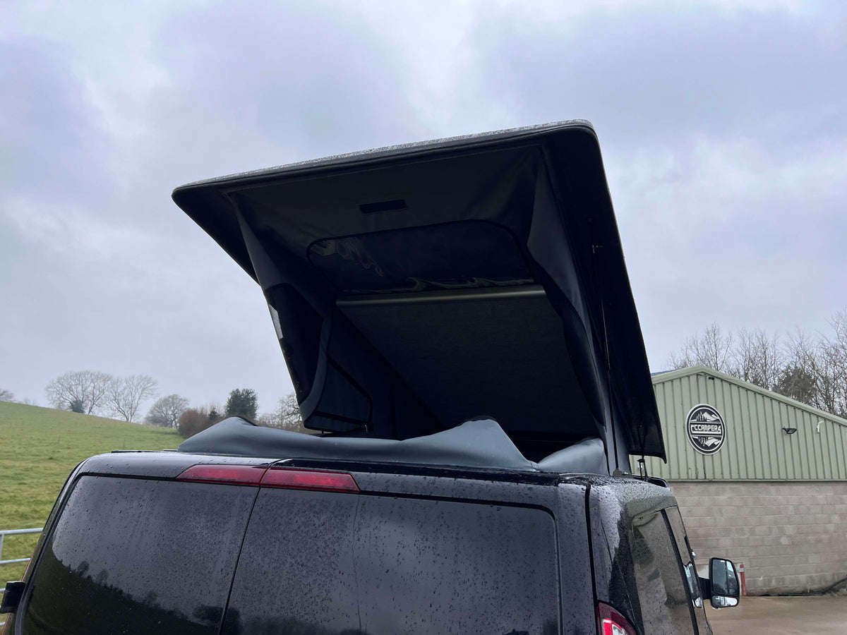 Black Ford Transit Custom pop-top roof raised, showing tinted rear window.