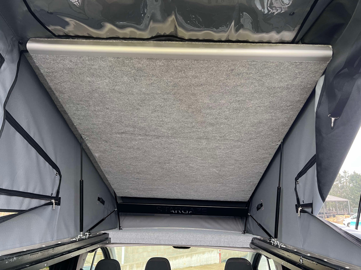 Pop-top roof interior with grey fabric ceiling panel and side mounting brackets.