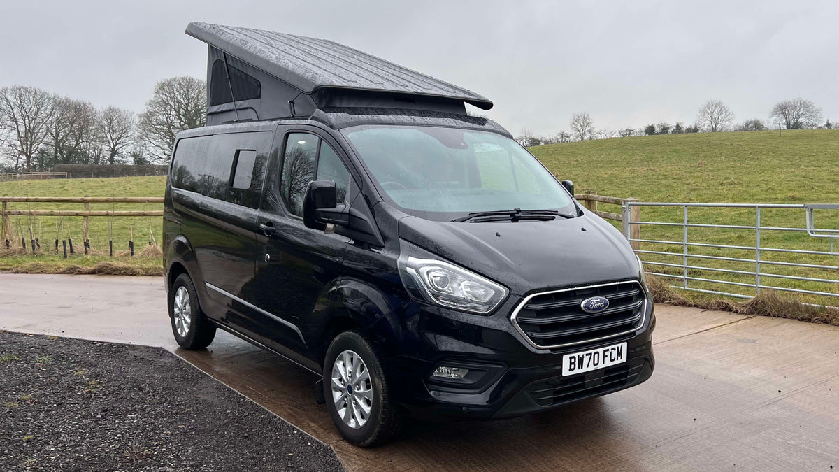 Black Ford Transit Custom van with pop-top roof closed, front grille and headlights.
