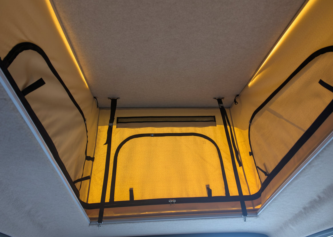 An overhead view of a Kia PV5 pop-up canopy tent with black straps and a bright interior light illuminating the underside.