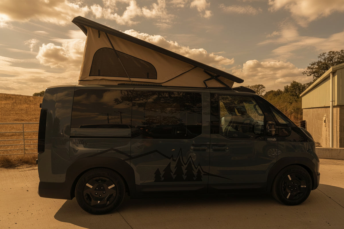 A Kia PV5 beige canvas pop top roof  camper van with a beige pop-up roof is parked outdoors on a concrete surface under a blue sky with clouds. A building and a blue vehicle are visible in the background.