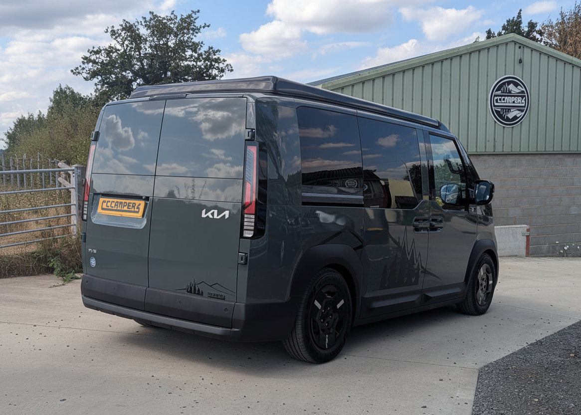 Dark Kia van with pop-top roof raised, rear side view