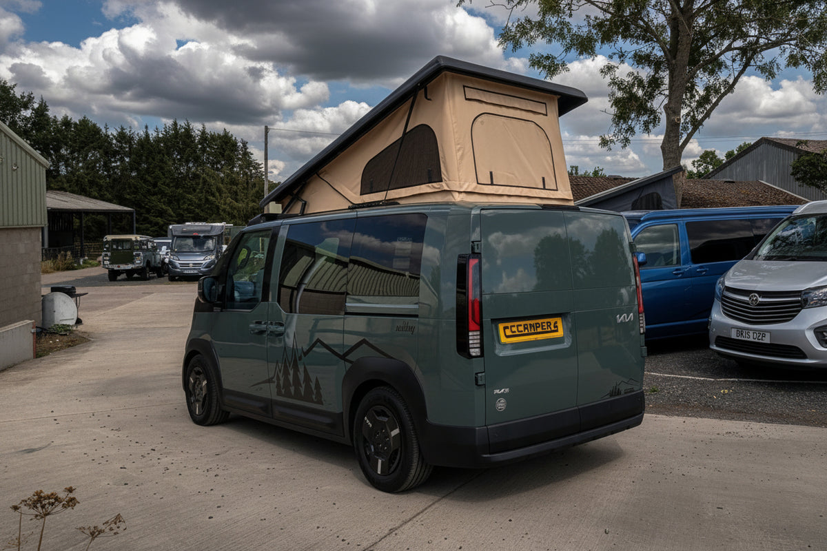 Pop-top camper roof raised on dark green Kia van, side and rear view