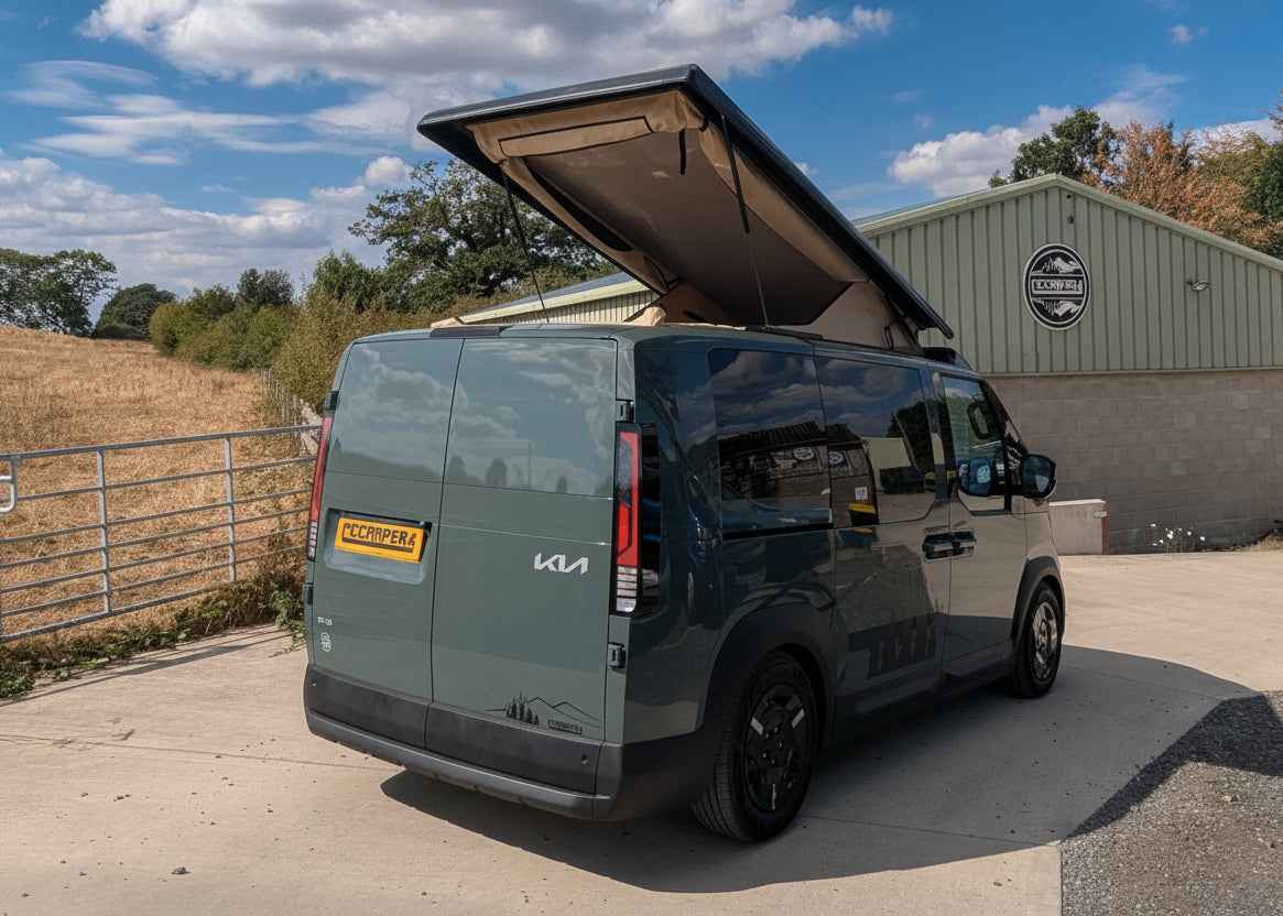 Dark Kia van with rear elevating pop-top roof raised, rear side view