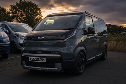 Dark Kia van with pop-top roof raised, front view at dusk