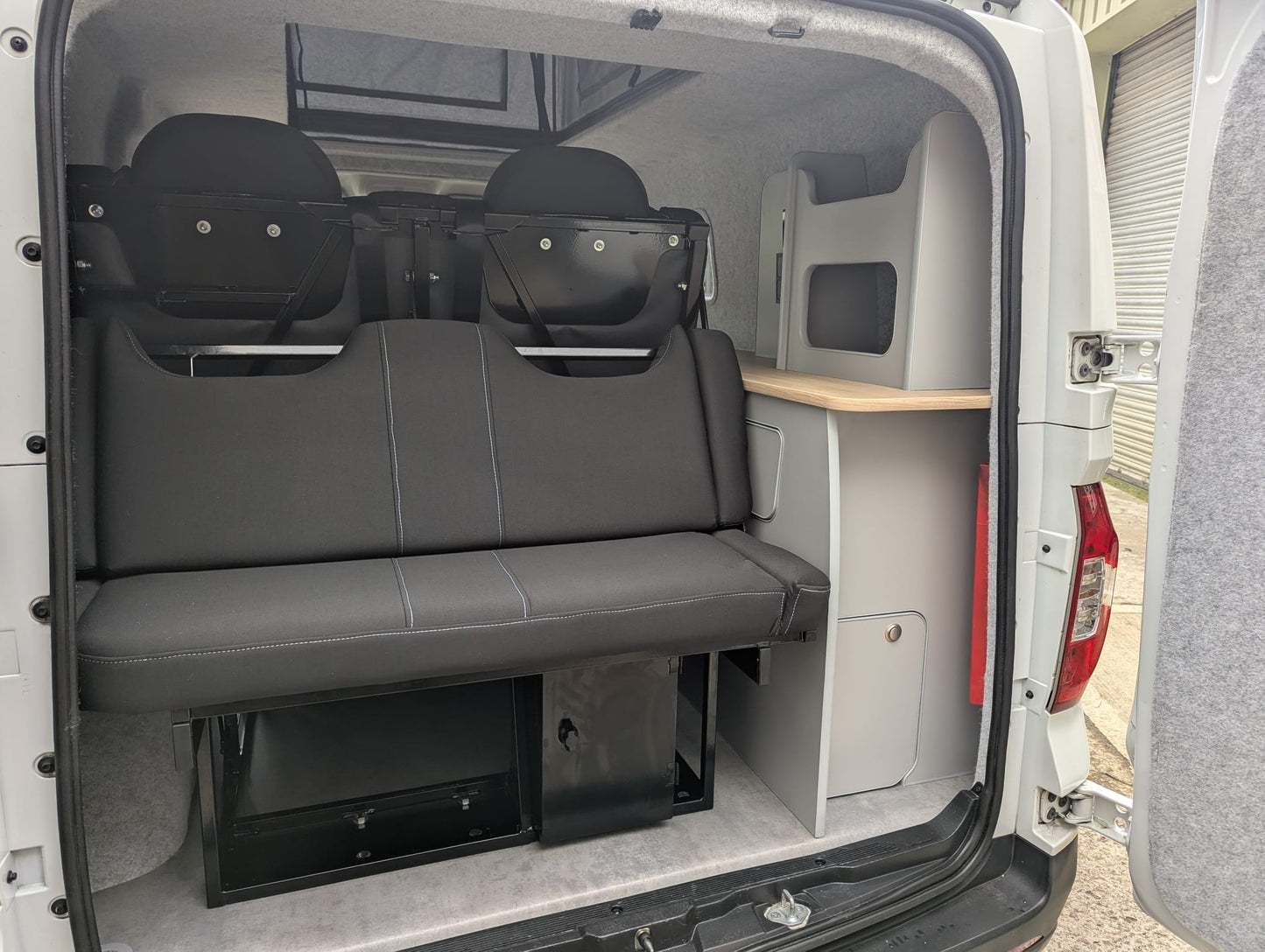 Maxus eDeliver 3 Ultimate Side Kitchen Layout Campervan Conversion interior with gray bench seat and storage compartments
