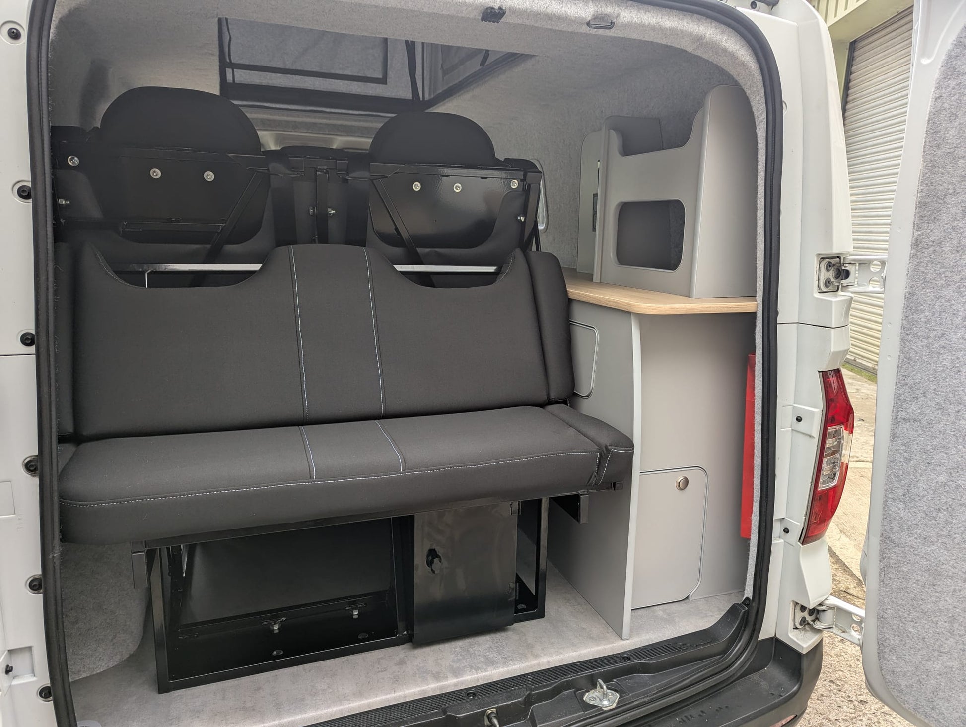 Maxus eDeliver 3 Ultimate Side Kitchen Layout Campervan Conversion interior with gray bench seat and storage compartments