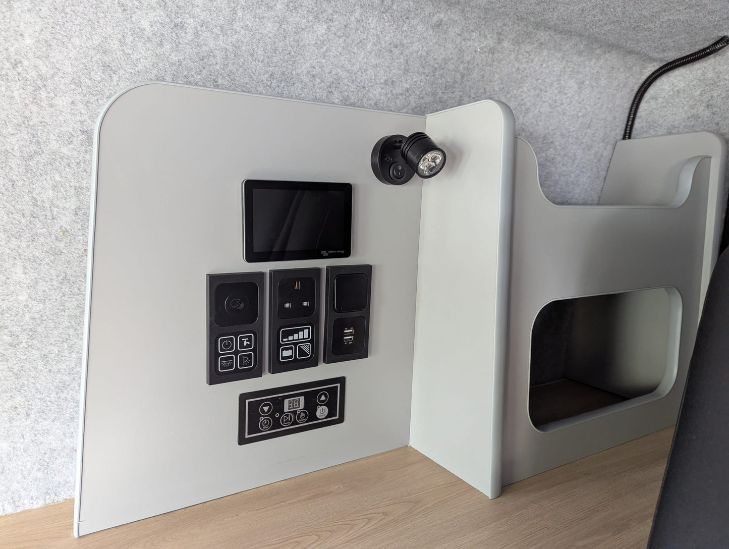 Gray electronic device with control panel on a wooden surface against a gray wall.