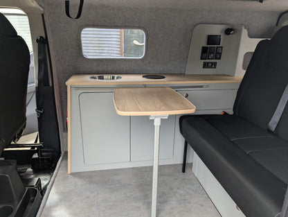 Compact kitchen area inside a Maxus eDeliver 3 Ultimate Side Kitchen Layout Campervan Conversion with a table, sink, and storage compartments.