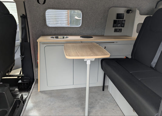 Compact kitchen area inside a Maxus eDeliver 3 Ultimate Side Kitchen Layout Campervan Conversion with a table, sink, and storage compartments.
