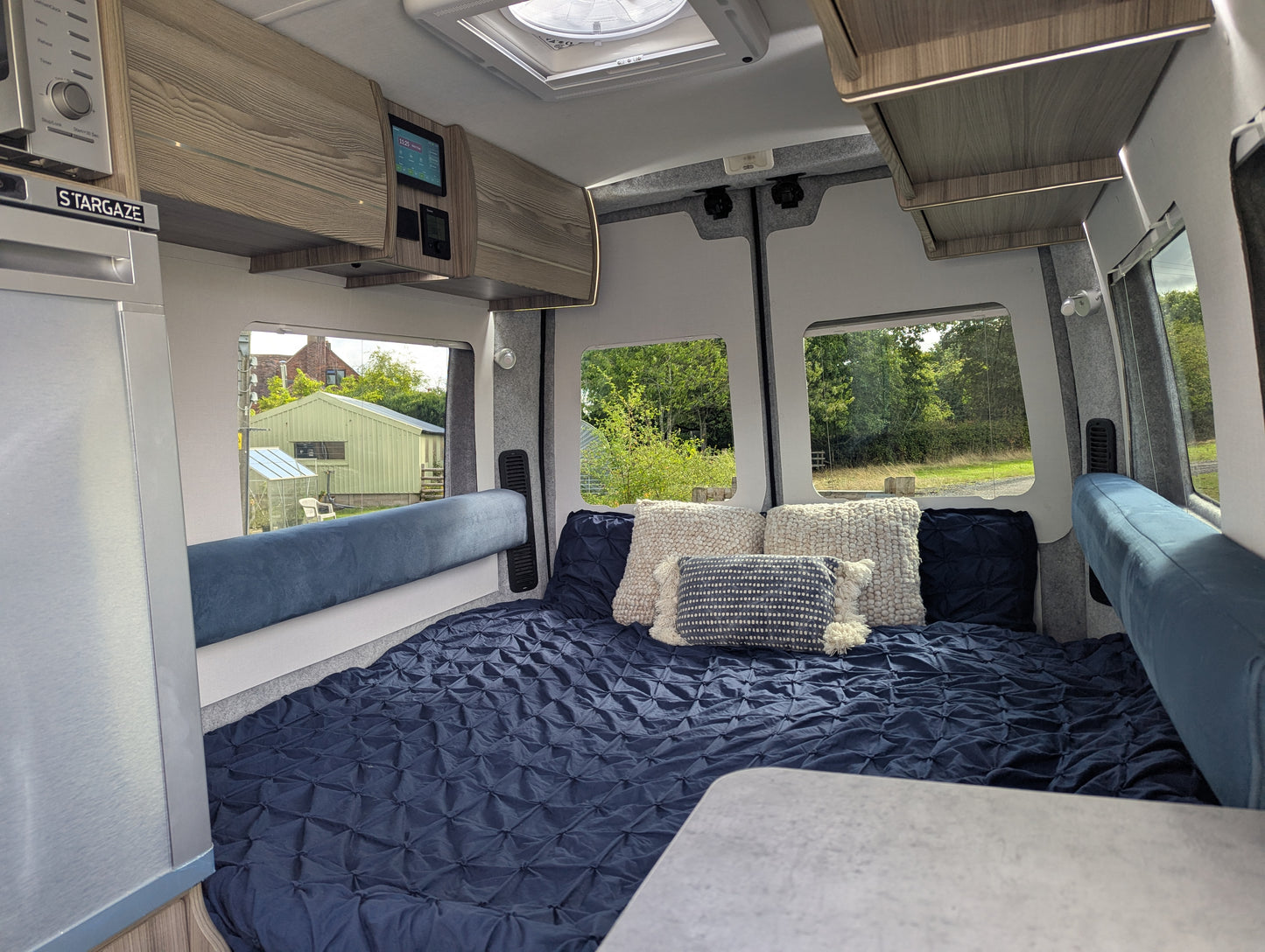 Interior of a renault master nissan interstar motorhome with a bed setup, cushions, and windows showing an outdoor view.