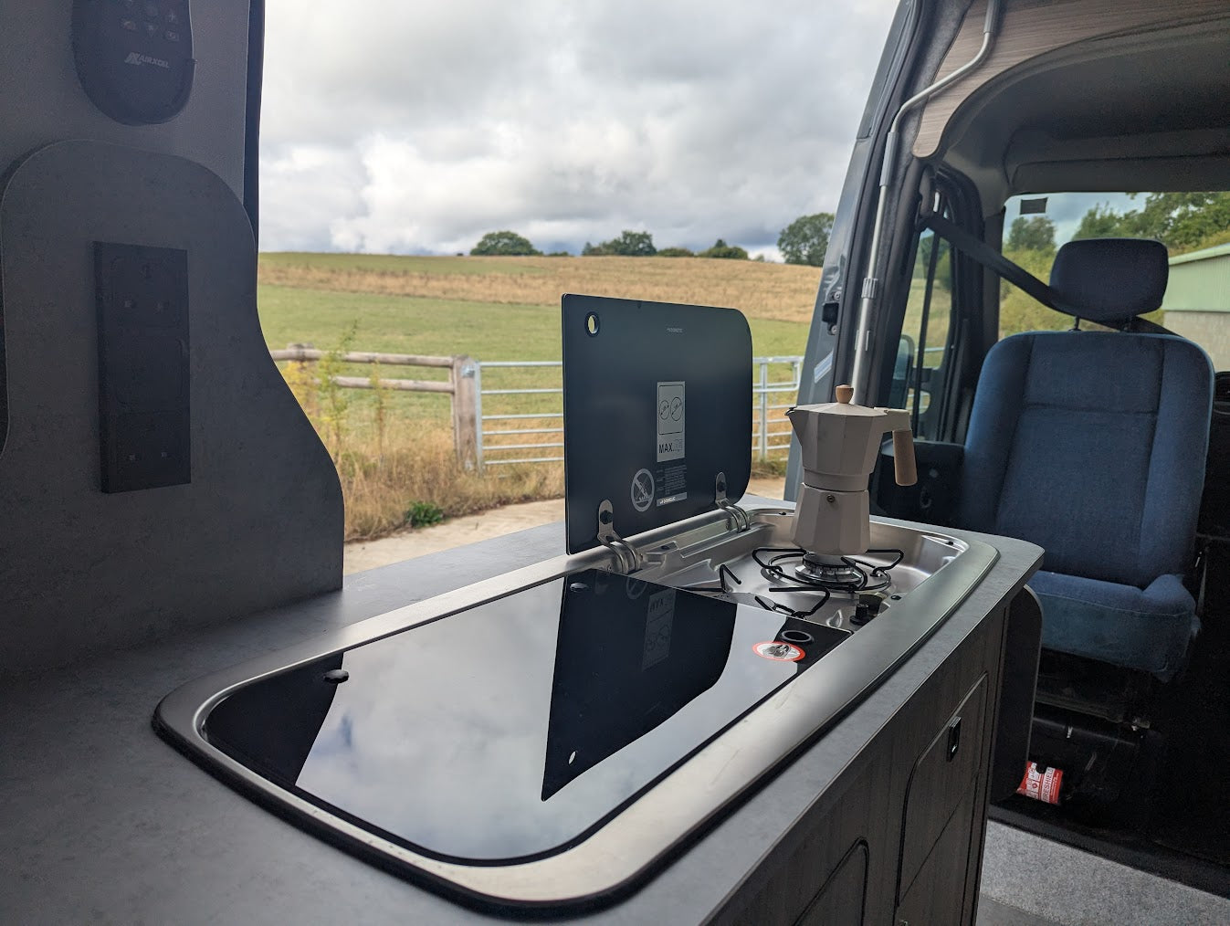 Renault master nissan interstar motorhome interior with a coffee maker on a stove, open door showing a field outside.