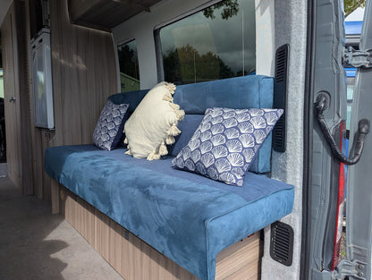 Blue bench with decorative pillows inside a vehicle, possibly a camper van.