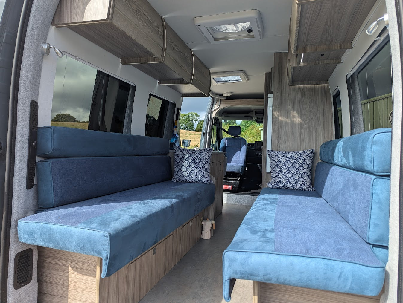 Interior of a van with blue upholstered seating and wooden paneling.