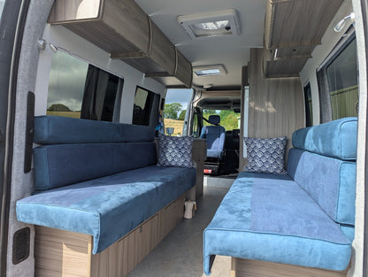 Interior of a van with blue upholstered seating and wooden paneling.