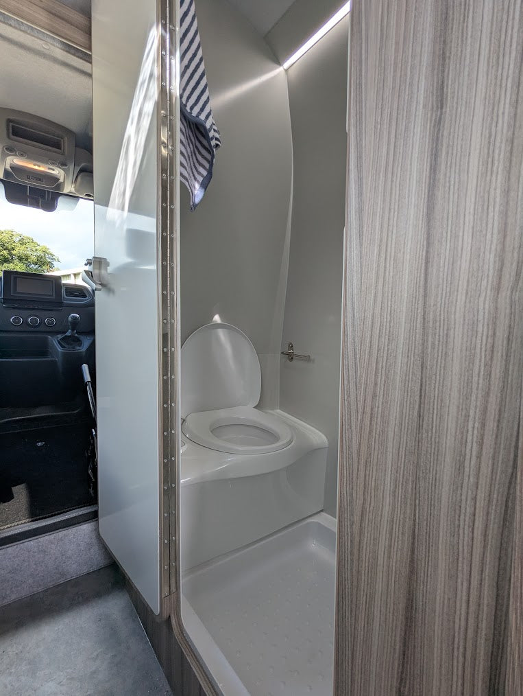Compact bathroom inside a vehicle with a toilet and shower area.