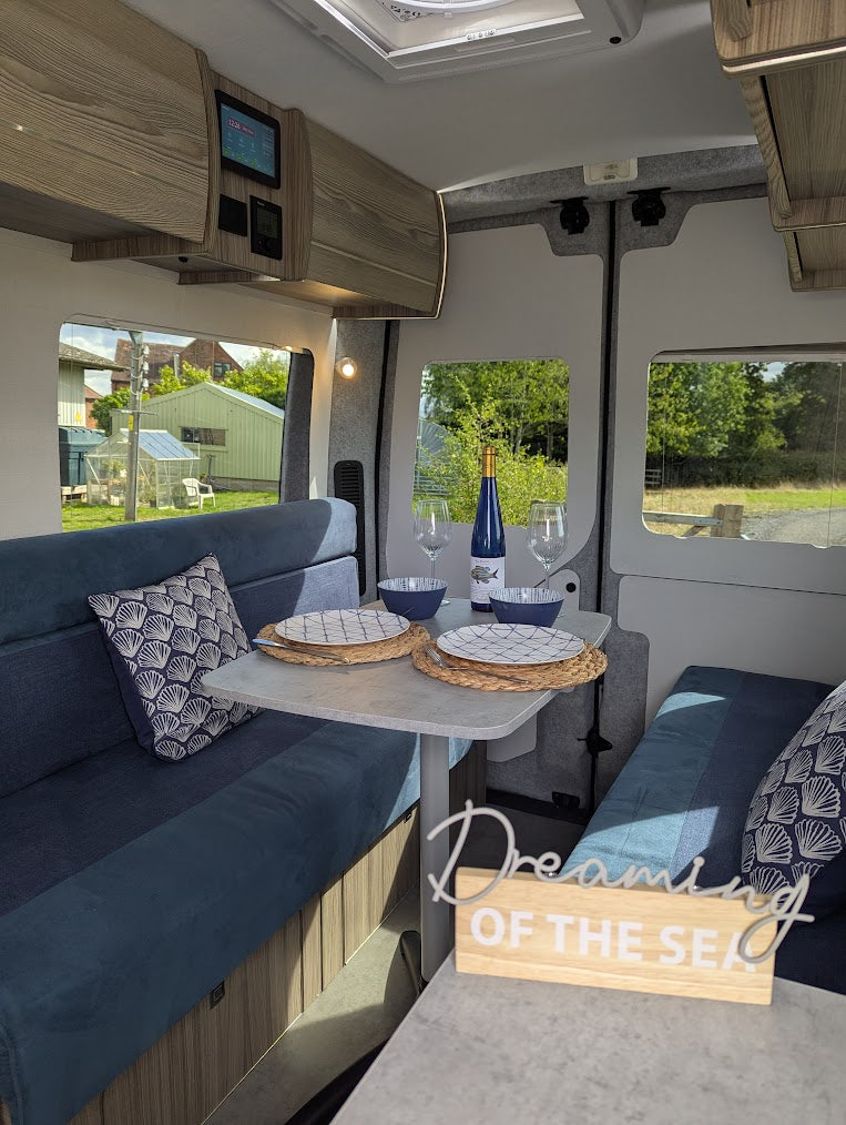 Interior of a camper van with blue seating, small table, and 'Dreaming of the Sea' sign.