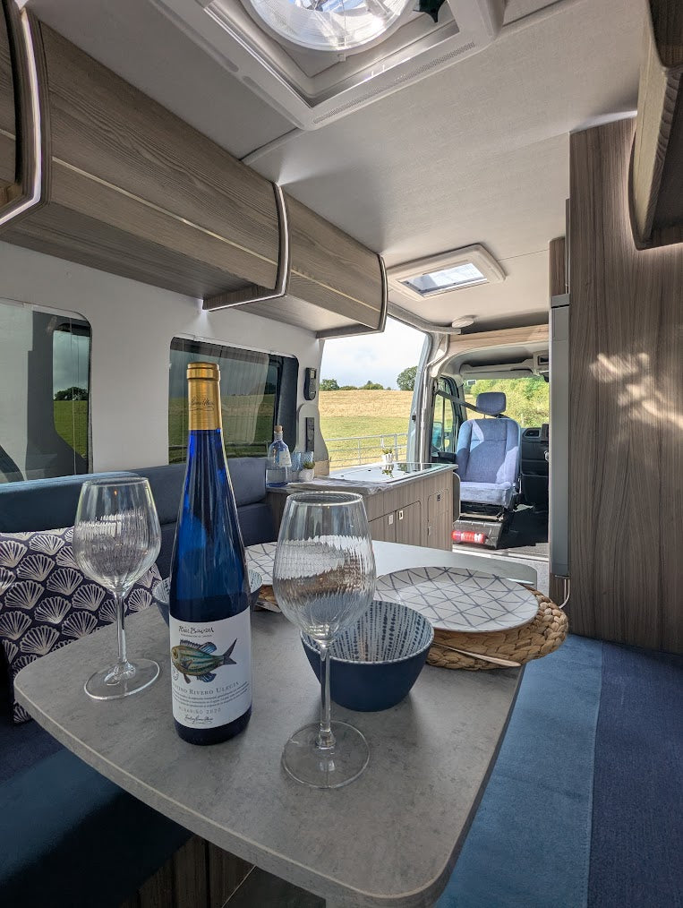 Interior of a vehicle with a bottle of wine, glasses, and a plate on a table.