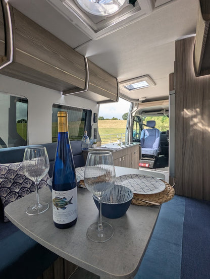 Interior of a vehicle with a bottle of wine, glasses, and a plate on a table.