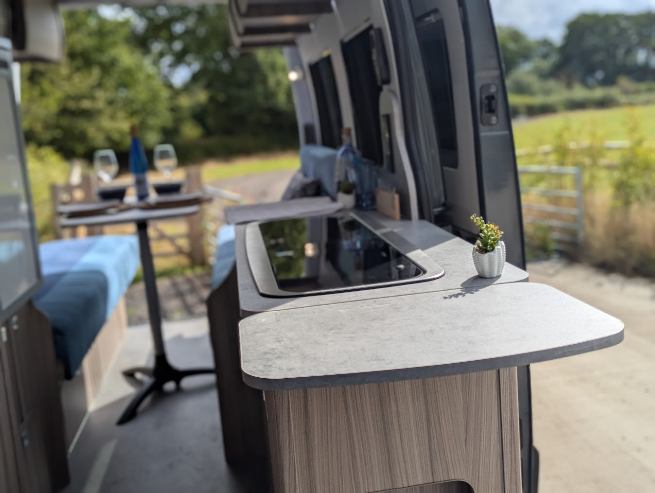 Camper van interior with a table and small plant, outdoor setting visible through the window.