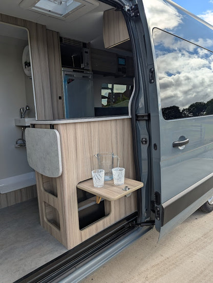 Interior of a van with wooden paneling, table, and kitchenette setup.