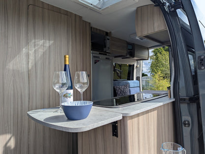 Cooking area inside a vehicle with a bottle, glasses, and bowl on a countertop.