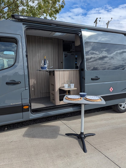 Gray van with open door revealing a small kitchen setup on a concrete surface.