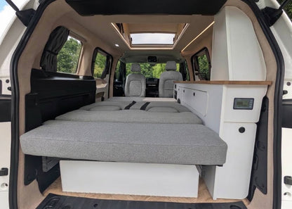 Campervan bed platform with grey mattress, white storage cabinet, and wood trim