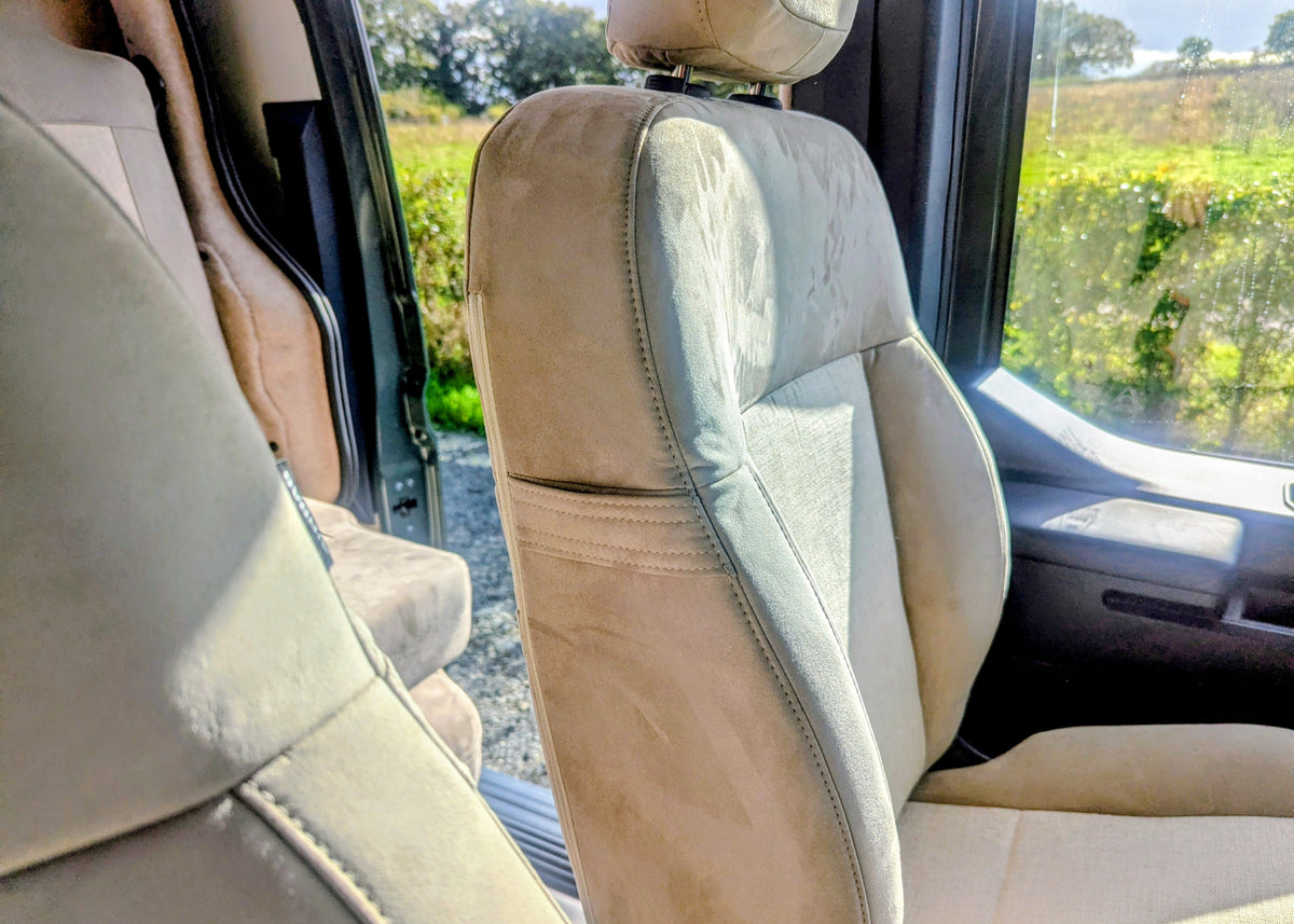 Side profile of the upholstered front passenger seat featuring premium beige suede and fabric trim inside the Kia PV5 Witley electric campervan. sunglasses holder