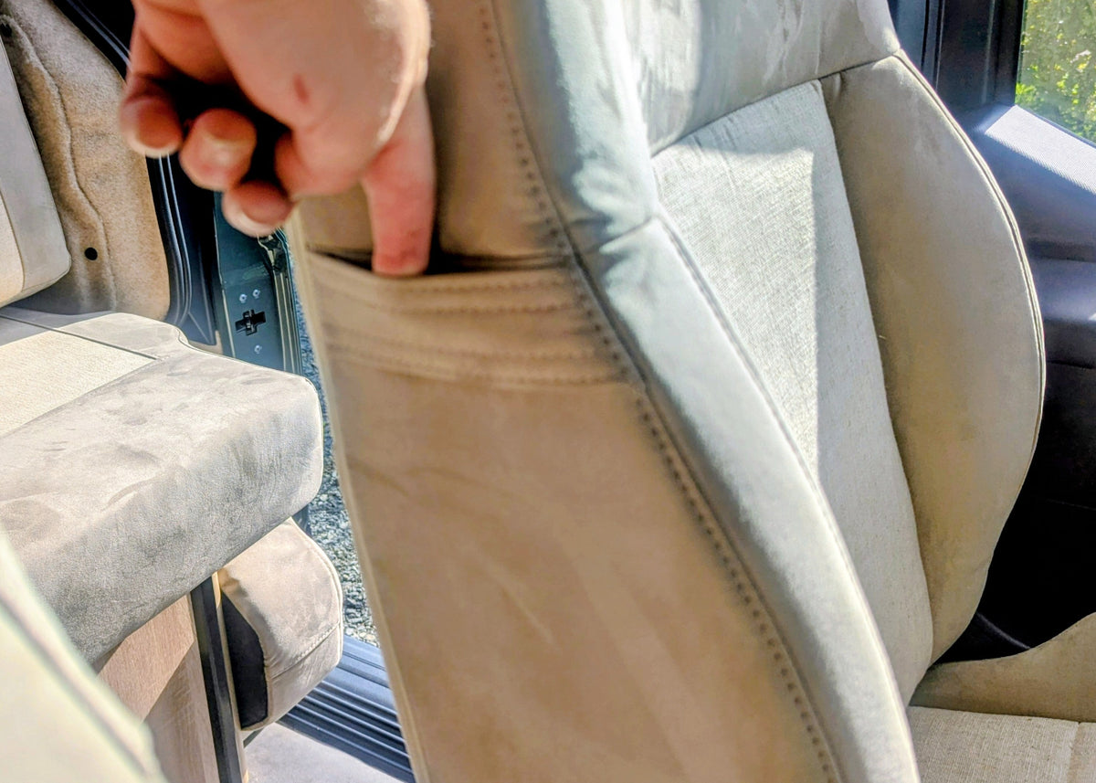 Close-up interaction showing the integrated storage pocket on the back of the front passenger seat inside the Kia PV5 Witley campervan.