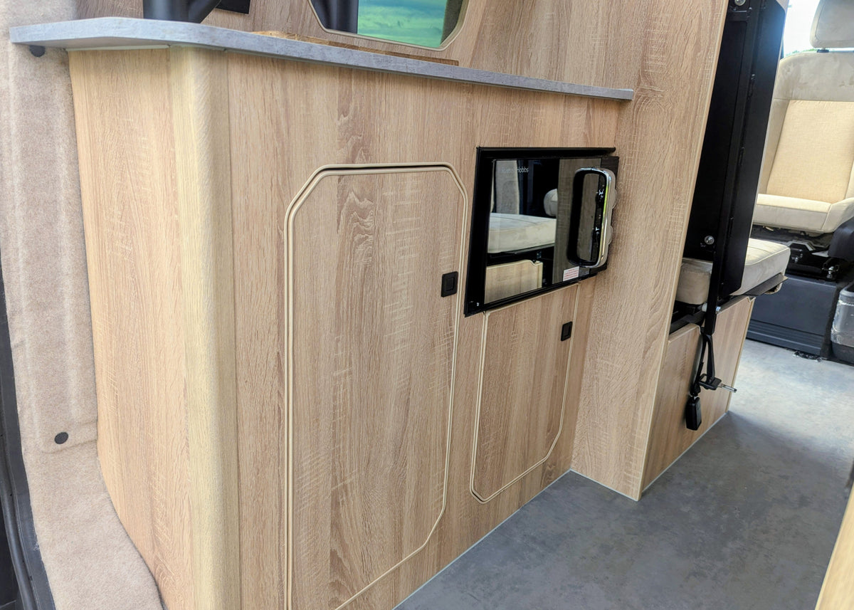 Side profile of the kitchen unit cabinetry in the Kia PV5 Witley campervan featuring closed overhead-style doors and an integrated compact microwave.