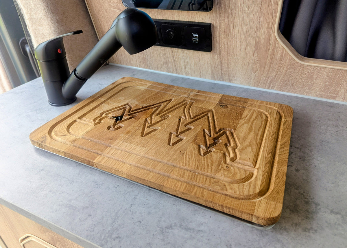Close-up of the custom wooden chopping board sink cover featuring laser-engraved mountain graphics on the kitchen counter of the Kia PV5 Witley campervan.