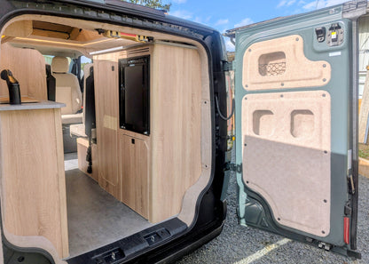 Open rear boot perspective showing the full-length interior layout, custom cabinetry, rear galley kitchen setup, and front cabin seats of the Kia PV5 Witley conversion.