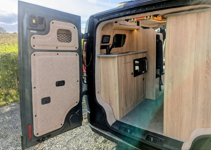 Custom interior trim lining and built-in storage net detail on the open rear double doors of the Kia PV5 Witley campervan conversion.