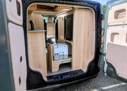 Rear storage garage area of the Kia PV5 Witley electric campervan featuring a custom pull-out slide holding a portable chemical toilet beneath the kitchen units.