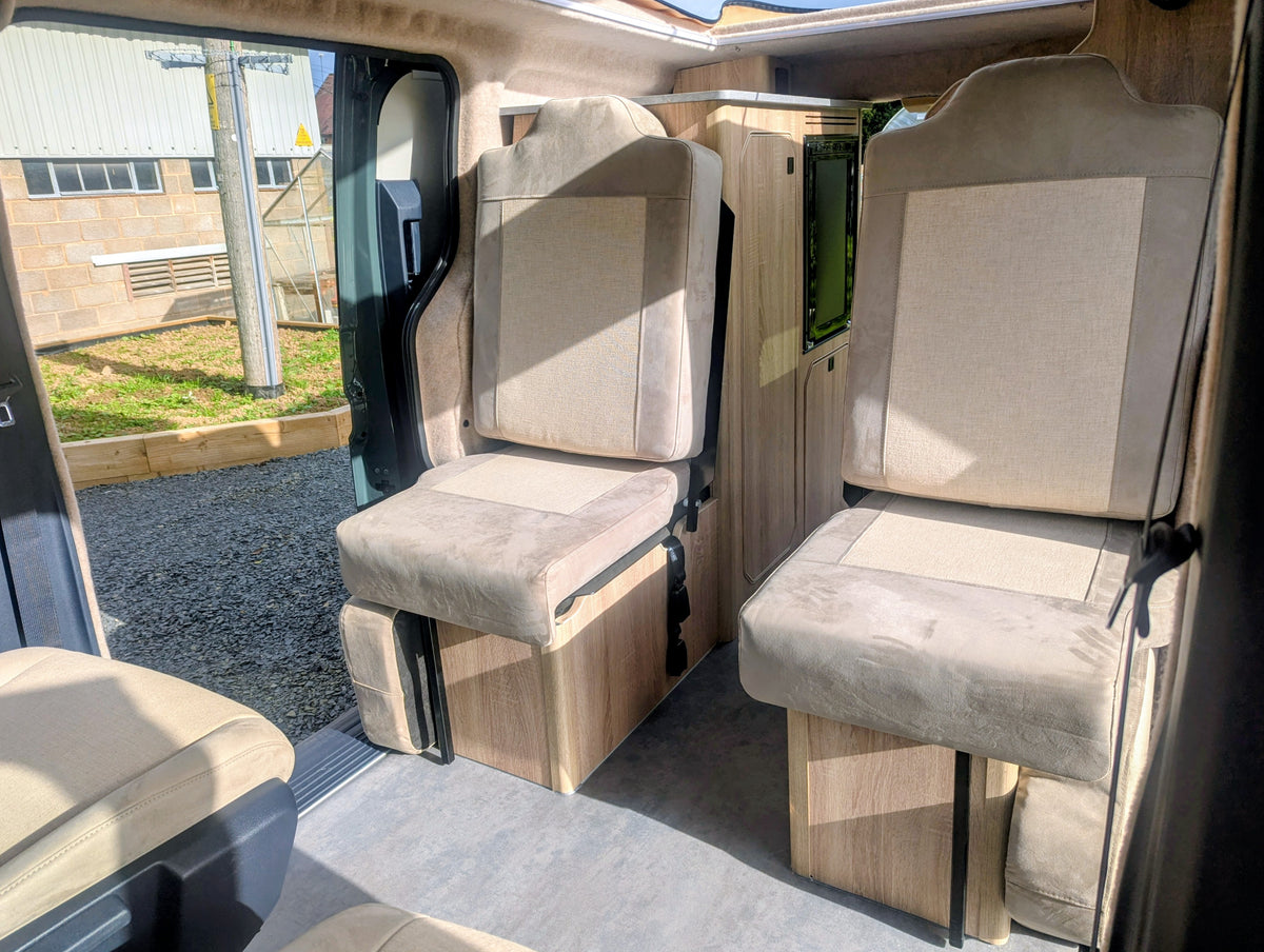 Interior view showing the Kia PV5 Witley campervan rear passenger seating layout and central walkway leading towards the front cabin.