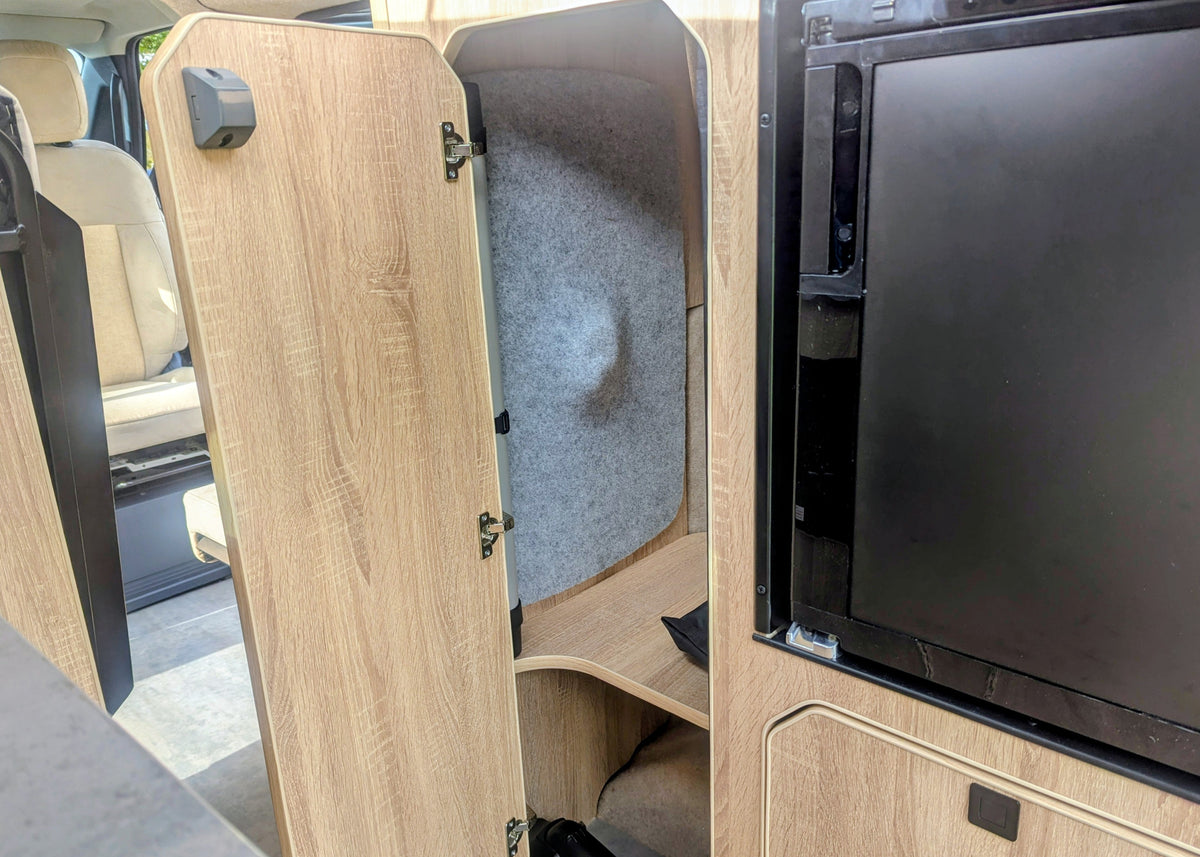 : Close-up of the open wardrobe storage locker inside the Kia PV5 Witley campervan featuring felt-lined acoustic walls and integrated wooden shelving.