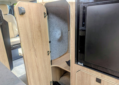 : Close-up of the open wardrobe storage locker inside the Kia PV5 Witley campervan featuring felt-lined acoustic walls and integrated wooden shelving.