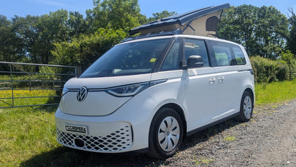 White Volkswagen van with a rooftop solar panel on a gravel road with greenery in the background