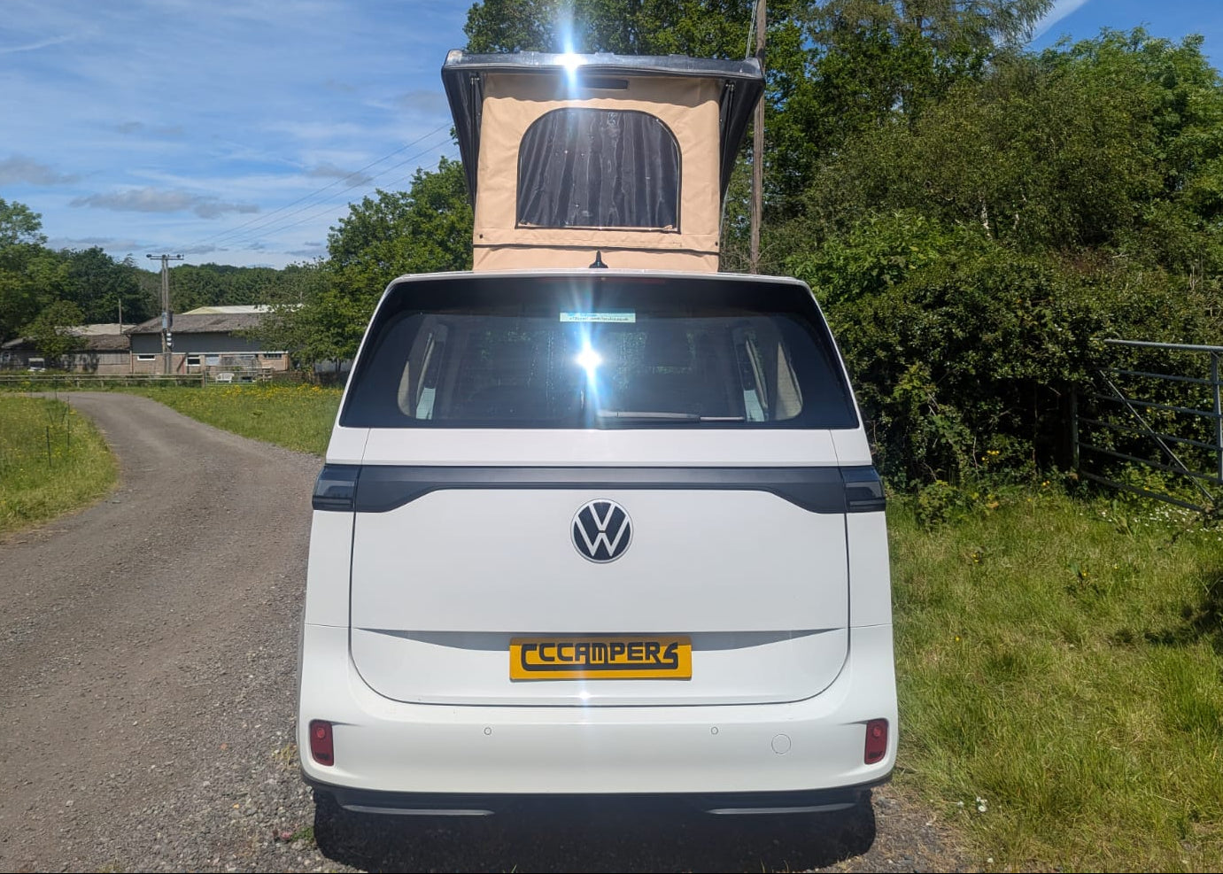 White Volkswagen van with a rooftop tent on a rural road.