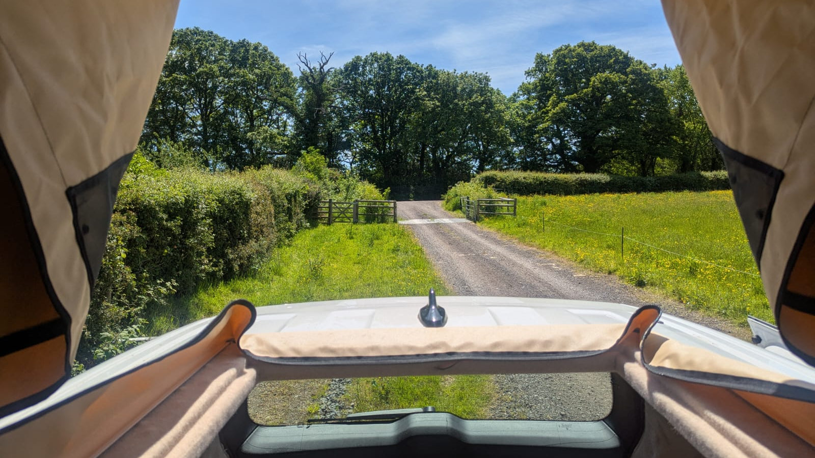 View from inside a vehicle with an open roof, showing a rural road and greenery.